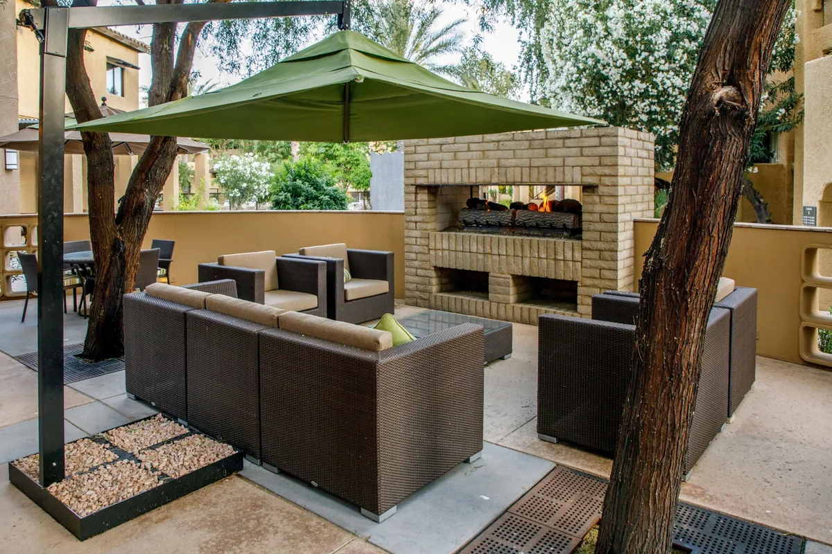 A sunny patio area with comfortable seating, a cozy outdoor fireplace, and a shade canopy surrounded by lush landscaping. Families are gathered together enjoying the friendly, communal setting ideal for relaxing after a day of exploring nearby attractions.