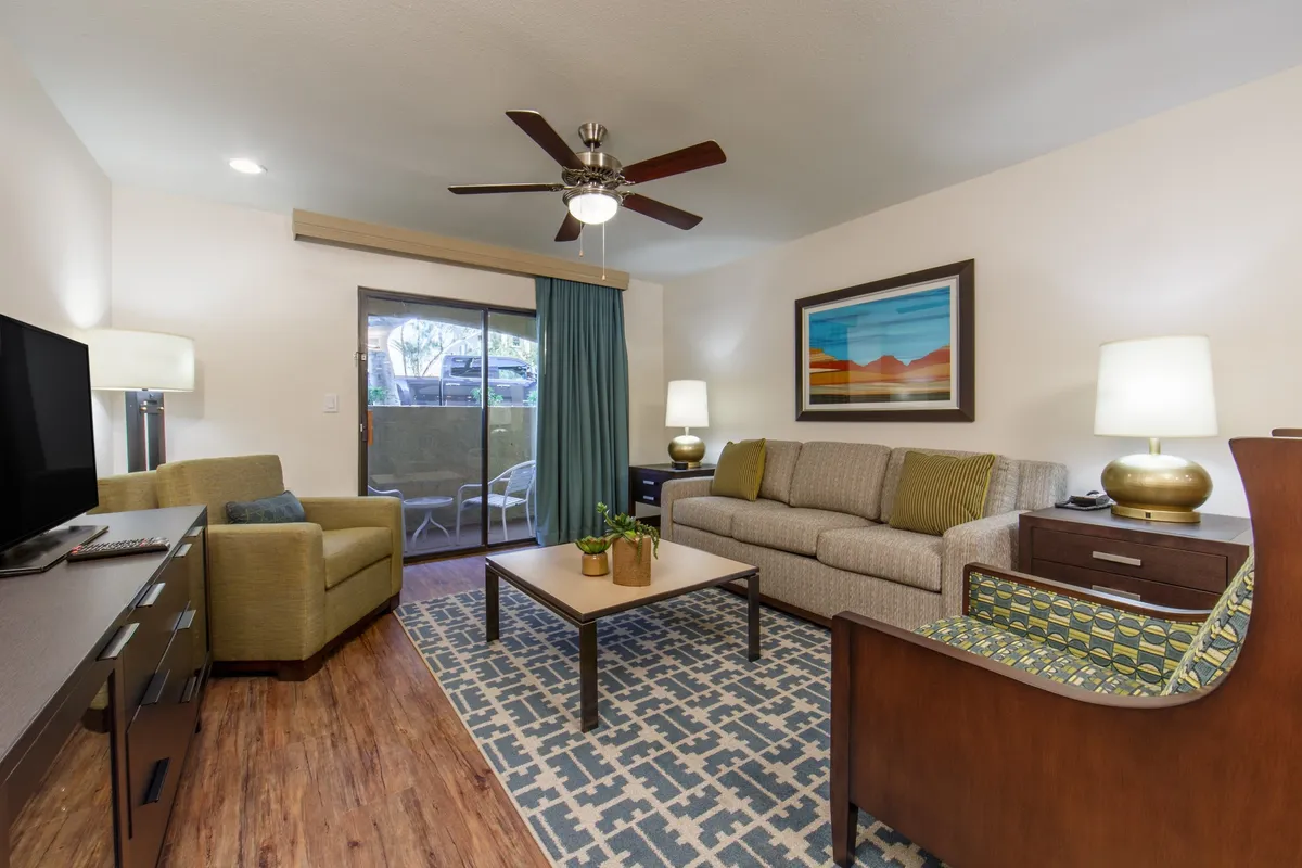 The image showcases a warm, inviting living room with a plush sofa, stylish coffee table, modern artwork on the walls, and soft curtains framing sunlit windows. The setting is designed for comfort, perfect for relaxing with family or hosting friends after a day of Scottsdale adventures.