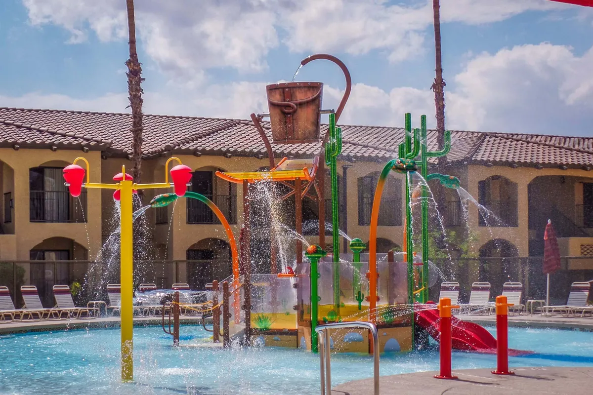 Brightly colored water slides and a lively splash pad take center stage in this energetic poolside scene. Children and families are clearly enjoying the water features, with loungers nearby for relaxation. The mood is joyful, highlighting fun-filled days under the sun, and the space is clearly designed for family memories.
