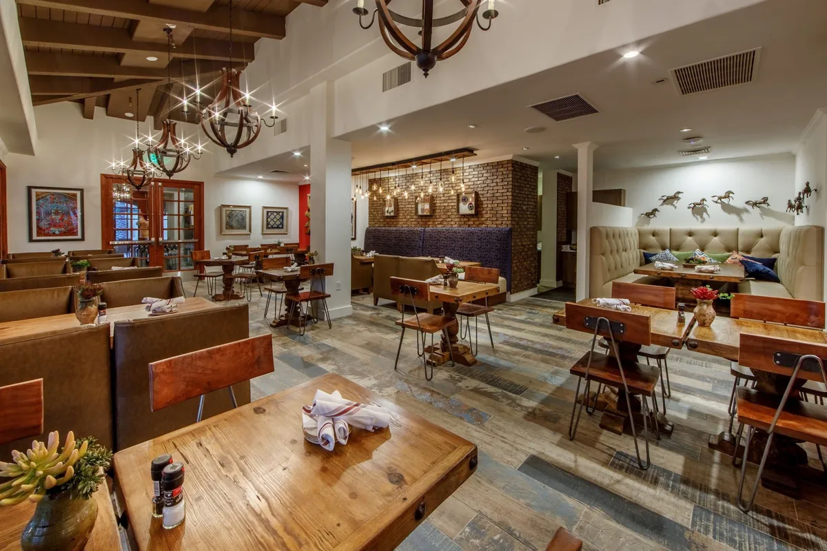 A cozy and stylish dining area with chandeliers overhead, wooden tables, comfortable seating, and decorative wall art. The space feels intimate yet versatile, perfect for both celebratory dinners and everyday meals, reflecting the convivial spirit of shared dining.
