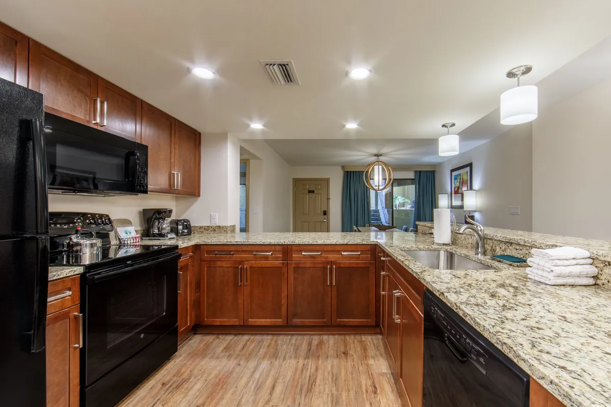 This image presents a welcoming kitchen space featuring granite countertops, dark wood cabinetry, and modern kitchen appliances. The lighting fixtures add warmth, creating an inviting atmosphere for cooking and entertaining. The scene evokes a sense of family gatherings and culinary creativity, with clear visibility of key kitchen elements such as the stove and ample counter space.